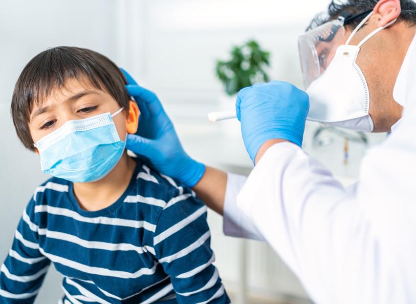 ENT doctor with mask on examines the inside of a child's ear
