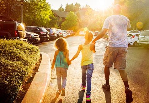 Man holding hands with two small daughters walking through the parking lot