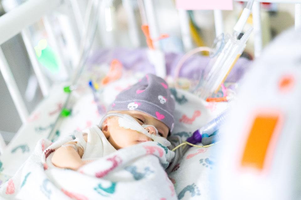 Baby in open crib in NICU with breathing support and hat